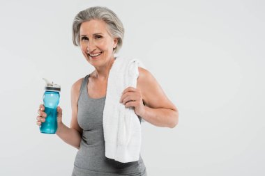 Omzunda beyaz havluyla, elinde spor şişesiyle, gri üzerinde su bulunan son sınıf öğrencisi memnun bir kadın. 