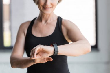 Siyah askılı neşeli son sınıf kadınının spor salonundaki spor salonundaki spor salonundaki spor takip cihazındaki aktiviteleri kontrol etmesi. 