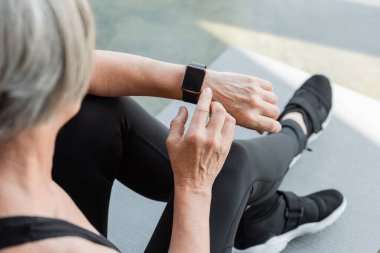 Spor salonunda spor yaptıktan sonra, gri saçlı, spor salonunda oturan ve spor takip cihazını kullanan son sınıf öğrencisinin en iyi görüntüsü. 