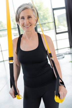 Siyah spor giyimli neşeli bir kadın spor salonunda askılarıyla egzersiz yapıyor. 