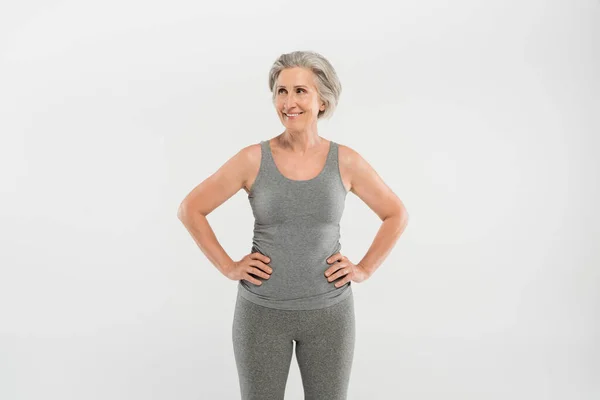 穿着运动服的快乐而年长的女人 双手放在灰色的臀部上站着 — 图库照片