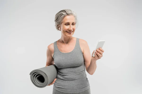 Wesoła Seniorka Bezprzewodowych Słuchawkach Matą Fitness Smartfonem Odizolowanym Szaro — Zdjęcie stockowe