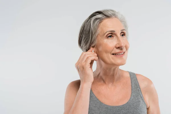 Happy Senior Woman Adjusting Wireless Earphone Isolated Grey — Stock Photo, Image