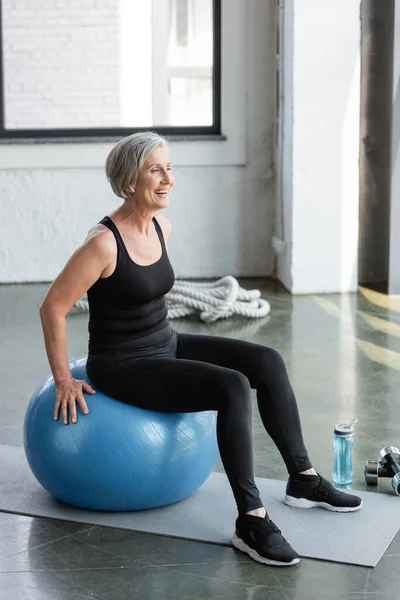 全身上下穿着黑腿和背心的老年女子在蓝色健身球上运动 — 图库照片