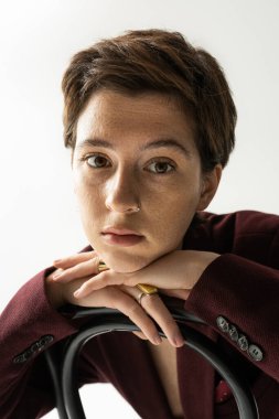 Kısa esmer saçlı, çilli kadının portresi gri arka planda kameraya bakıyor.