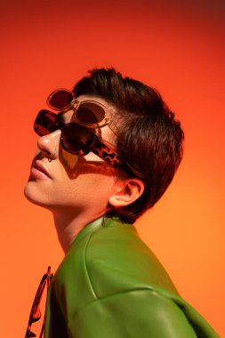 portrait of young woman with short brunette hair wearing two trendy sunglasses on orange background clipart