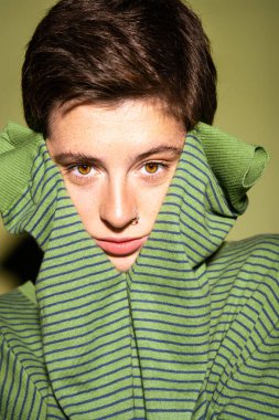 portrait of pensive freckled woman in striped pullover looking at camera on green background clipart