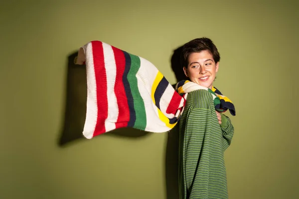 緑の背景に風になびく縞模様の多色のスカーフを見る陽気な女性 — ストック写真