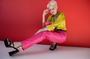 Moda topuklu sandaletleri ve güneş gözlükleriyle Carmine Pembesi 'nde poz veren dövmeli albino modeli. 