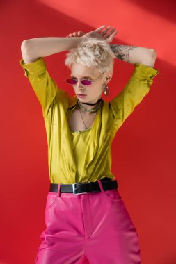 Dövmeli sarışın kadın şık bluzuyla poz veriyor ve Carmine Pembe 'de son moda güneş gözlüğü takıyor. 