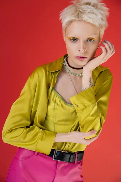portrait of tattooed albino model with yellow eyeliner looking at camera on carmine pink
