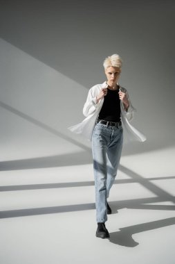 Gri arkaplanda beyaz gömlek giyen siyah kolsuz tişörtlü albino kadın.