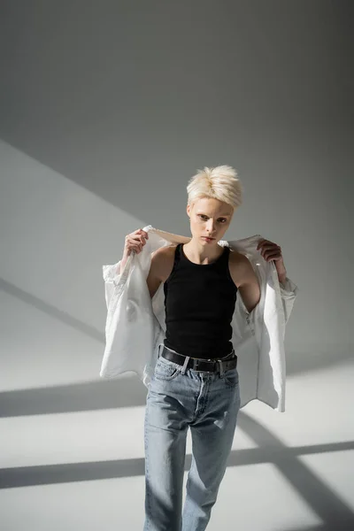 albino woman in black tank top and jeans wearing shirt on grey background
