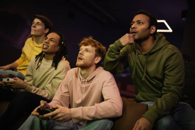 KYIV, UKRAINE - 13 Şubat 2023: Siber kulüpte video oyunu oynayan çok ırklı arkadaşlarının yanında oturan odaklanmış Hintli adam 