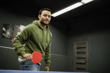 Oyun kulübünde masa tenisi oynayan odaklanmış Hintli adam. 