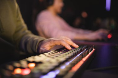 Siber kulüpte ışıklandırmalı bilgisayar klavyesi kullanan adamın kırpılmış görüntüsü 