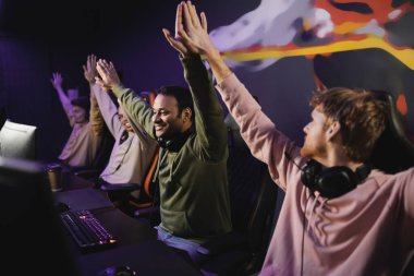 Cheerful indian player giving high five to friends near computers in cyber club  clipart