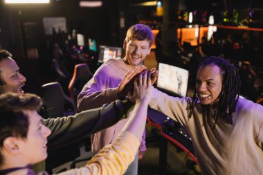 High angle view of positive multiethnic friends giving high five in gaming club  clipart