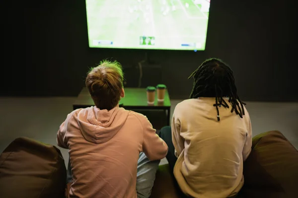 在网吧里 跨种族朋友们在模糊的咖啡边观看体育比赛的倒影 — 图库照片