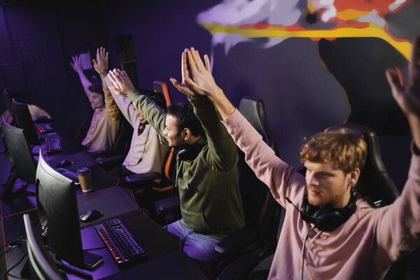 Smiling indian man giving high five to friends near computers in gaming club 