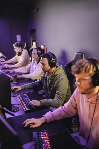 stock image Indian man in headphones playing video game on computer near interracial team in gaming club 
