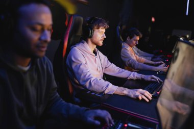Siber kulüpte bilgisayar başında bilgisayar başında çok ırklı bir takım oyunu oynayan kulaklıklı bir oyuncu 