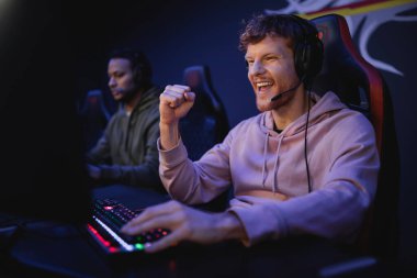 Kulaklıklı heyecanlı oyuncu siber klüpte bilgisayarın yanında evet işareti gösteriyor. 