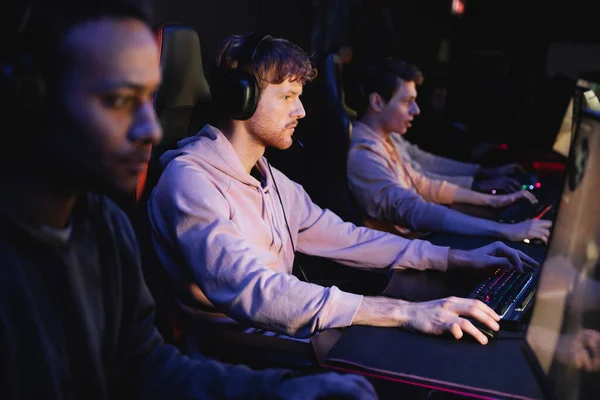 stock image Young man in headphones playing video game on computer near blurred interracial team in gaming club 