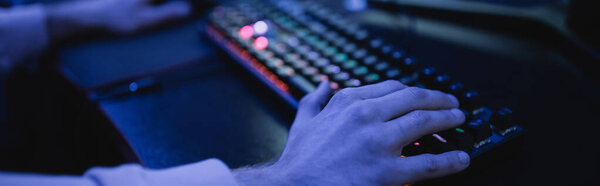Cropped view of man using keyboard in cyber club with lighting, banner 