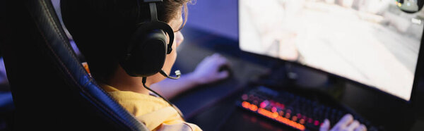 Gamer in headphones playing video game on computer in cyber club, banner 