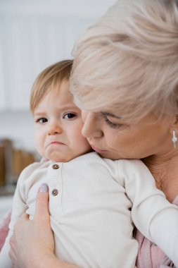 Büyükanne evde üzgün küçük kızı sakinleştiriyor ve kucaklıyor.