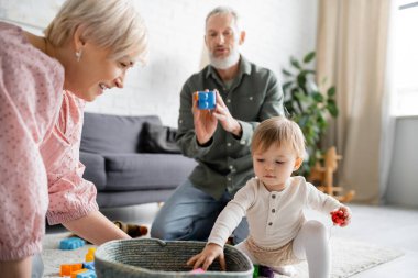 mature couple playing with granddaughter near wicker basket in living room clipart