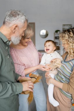 Oyuncak arabalı heyecanlı kız annesinin yanında gülüyor ve oturma odasında büyükannesi ve büyükbabası gülümsüyor.