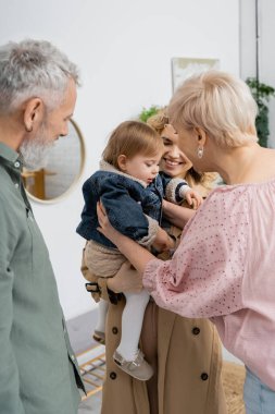 mature couple meeting daughter with little girl in denim jacket at home clipart