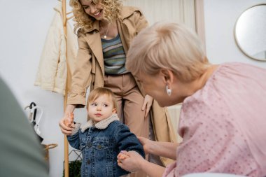 middle aged woman holding hand of granddaughter in denim jacket while meeting at home clipart