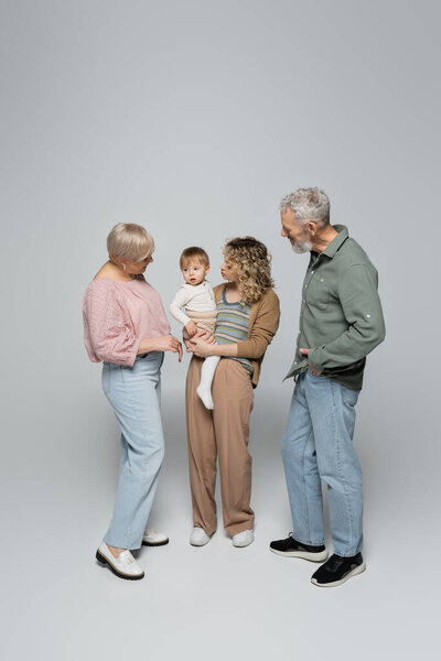 full length of woman holding little daughter near happy parents on grey background