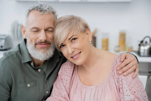 Happy Bearded Man Closed Eyes Embracing Wife Smiling Camera Kitchen — Stock Photo, Image