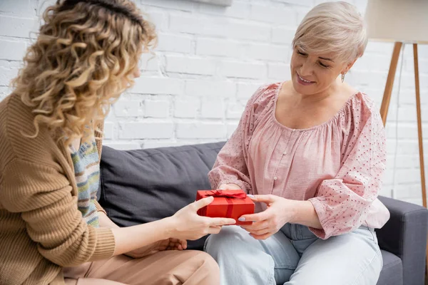 Curly Woman Presenting Gift Pleased Mother While Sitting Couch Home — Stock Photo, Image