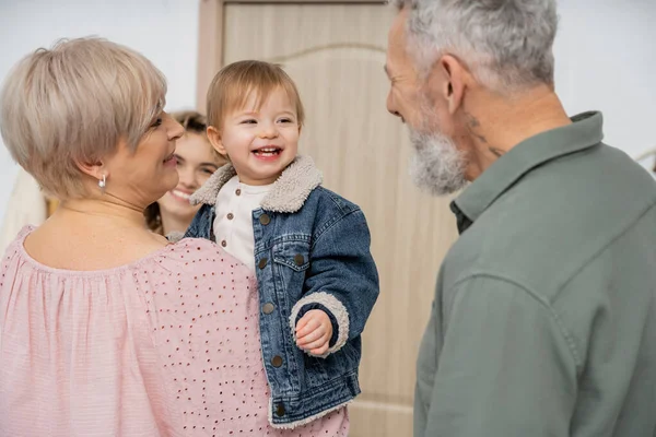 お母さんと幸せな祖父母の家のホールで笑っているデニムジャケットの屈託のない子供 — ストック写真