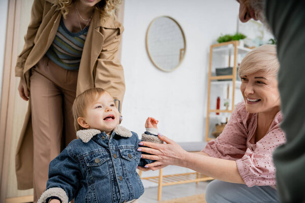 little girl in denim jacket smiling near mother and happy granny while meeting at home