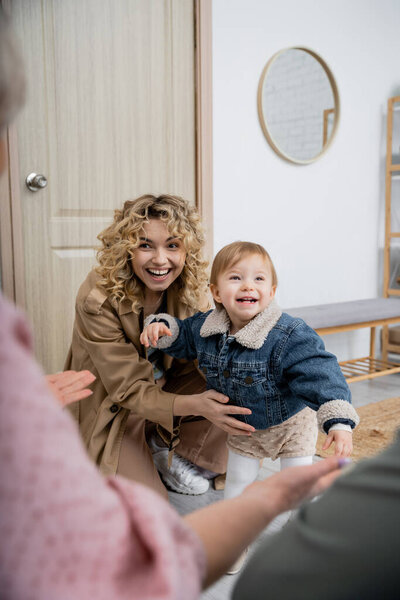 happy woman in trench coat and carefree girl in denim jacket visiting parents at home