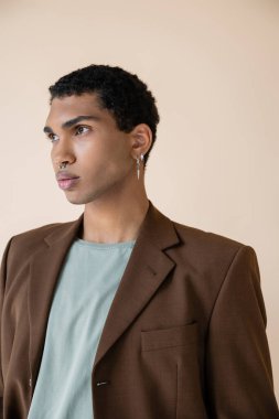 Genç ve şık Afro-Amerikalı gümüş piercingli adam bej rengi elbisesinden uzak duruyor.