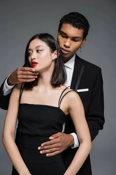 若いアフリカ系アメリカ人男性が優雅なアジア人女性の顎に触れグレーに孤立した赤い唇で — ストック写真