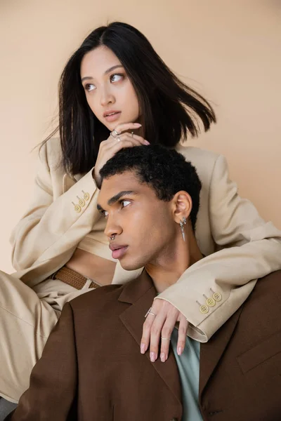 穿着西装的时髦的跨种族夫妇 在米色上看起来孤立无援 — 图库照片
