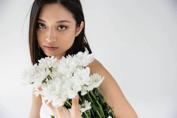 色彩艳丽的亚洲女人的肖像 自然妆容 在灰色孤立的白色花朵的花束旁边看着相机 — 图库照片