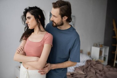 Sakallı adam, yatak odasında pijamalı mutsuz kız arkadaşını sakinleştiriyor. 