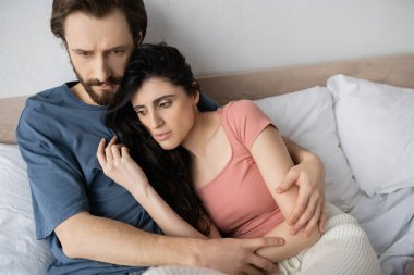 Evde yatakta yatarken pijama giymiş üzgün bir çift sarılıyor. 