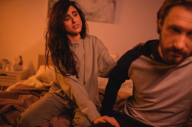 Üzgün esmer kadın gece yatakta bulanık erkek arkadaşına dokunuyor. 