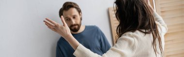 Brunette woman quarrelling with sad blurred boyfriend at home, banner  clipart