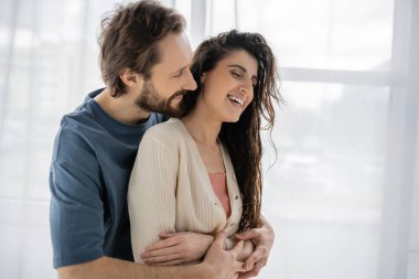Sakallı adam, evinde aşırı neşeli esmer kız arkadaşını kucaklıyor. 